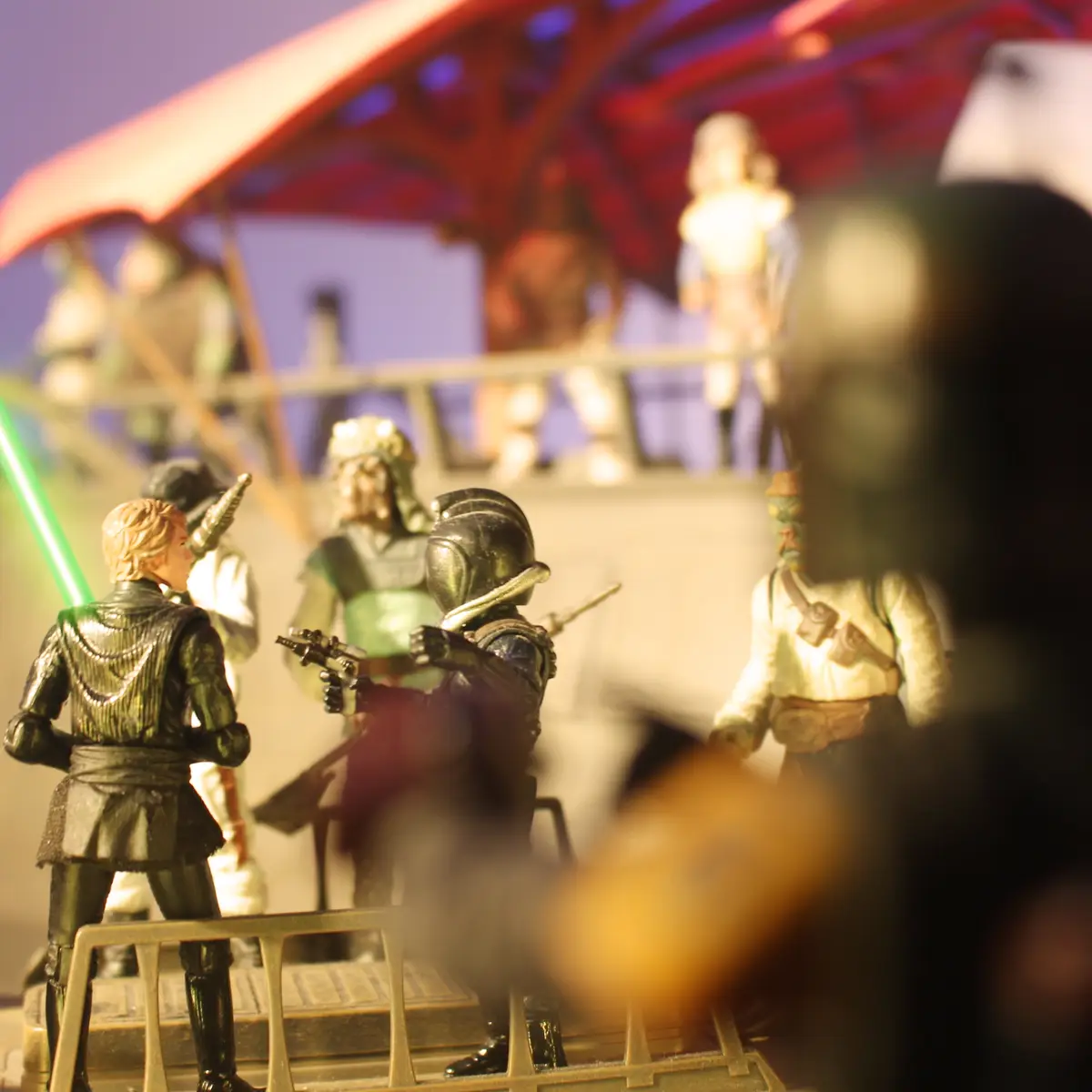 A shallow depth-of-field photo shows Star Wars action figures on a diorama, with a green lightsaber visible. The foreground…