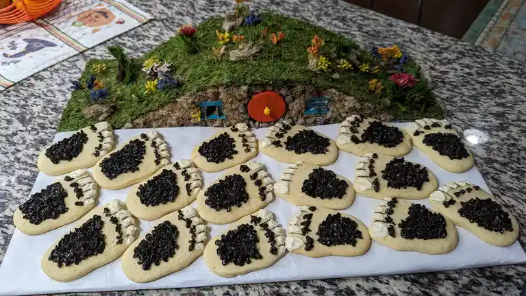 A tray of light-colored cookies shaped like human feet, decorated with white icing and black icing to resemble muddy…