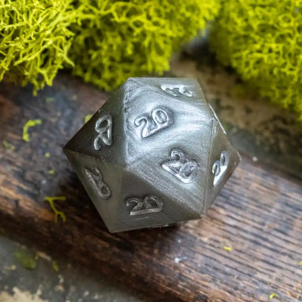 A dark gray, metallic twenty-sided die (d20) rests on a weathered wooden surface, surrounded by bright green moss. The die…