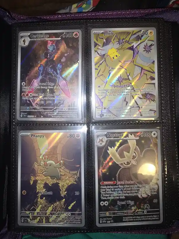 Four Pokémon trading cards are displayed in a binder: Ceruledge (HP 140), Joltik (HP 30), Phanpy (HP 80), and Noctowl (HP…