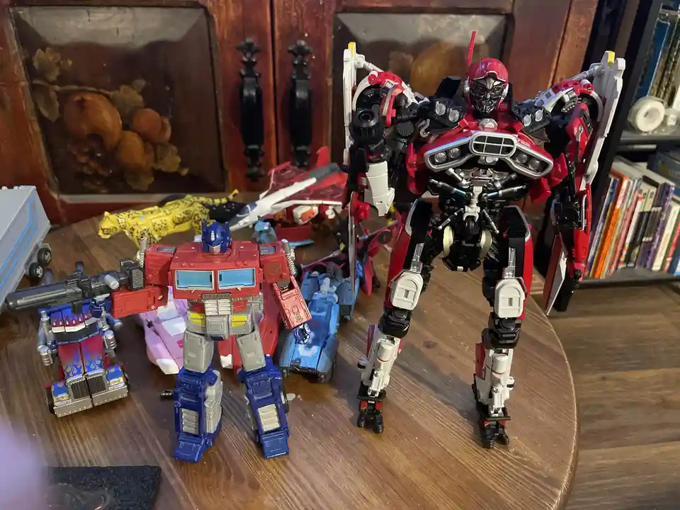 A collection of Transformers action figures is displayed on a wooden table, featuring Optimus Prime and a large red and…