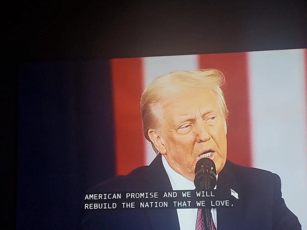 A close-up image of Donald Trump speaking into a microphone, with an American flag visible behind him. The overlaid text…