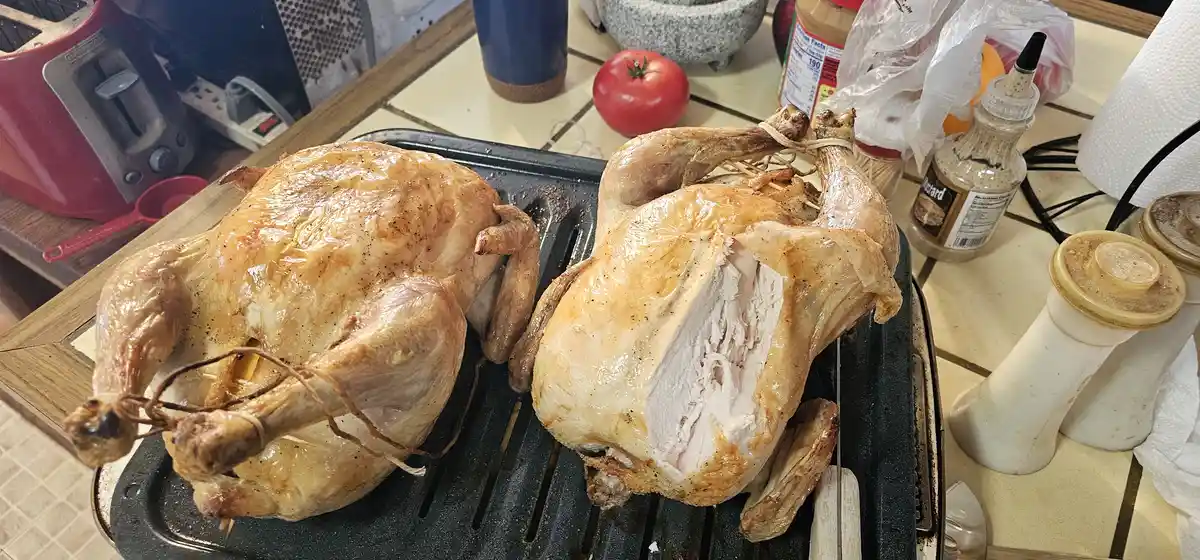 Two roasted chickens sit on a black grill pan on a kitchen counter. The chicken on the left is whole and intact, while the…