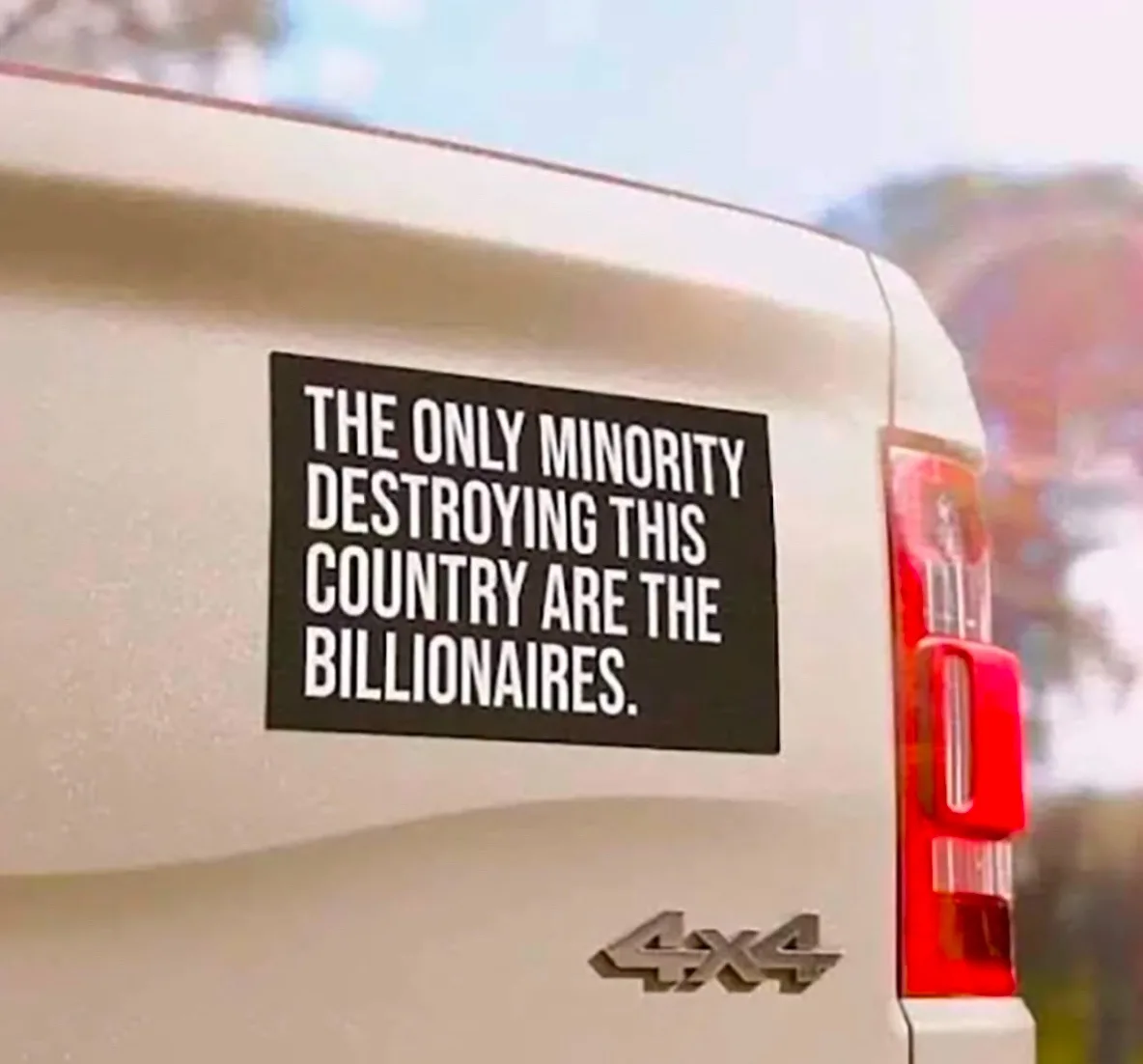 A close-up shot of the rear of a light-colored 4x4 truck, showing a black rectangular sticker with white text that reads…