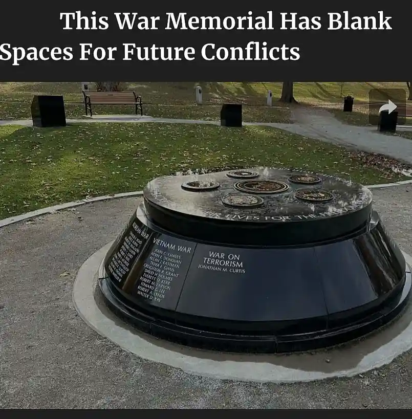 A black, circular war memorial in a park features engraved sections for 'KOREAN WAR', 'VIETNAM WAR', and 'WAR ON TERRORISM'…