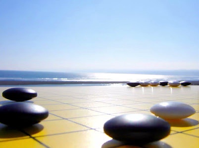 A serene beach scene with smooth black and white go stones arranged on yellow tiled pavement near the shoreline, under a…