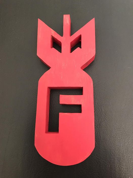 A red, 3D-printed or carved object shaped like a bomb, with the letter 'F' cut out in the center and two angular cutouts…