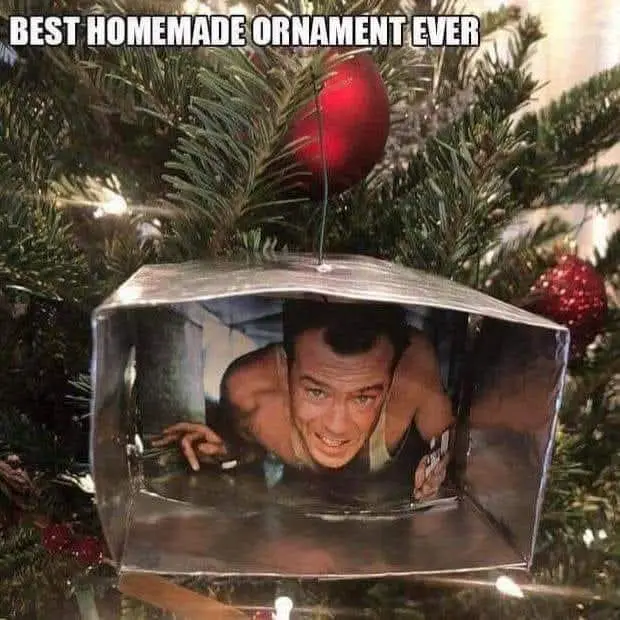 A close-up of a Christmas tree ornament made from a clear plastic box containing a printed photo of a shirtless man with a…