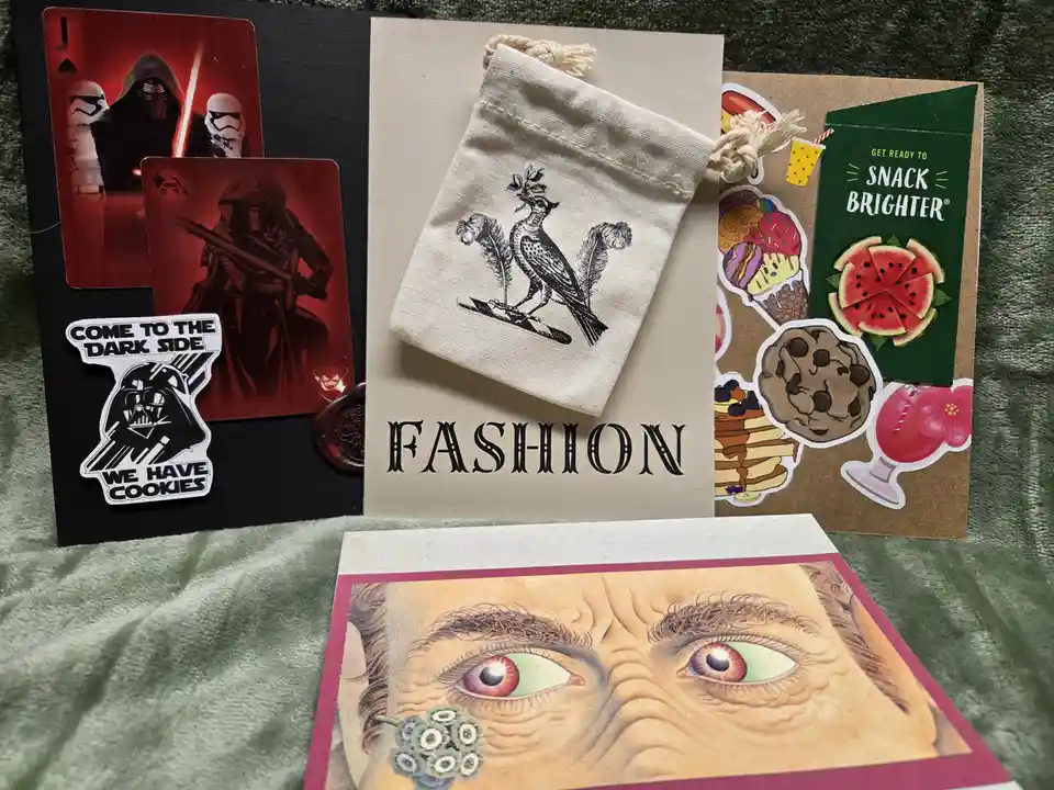 A flat lay of assorted items including Star Wars-themed playing cards and a Darth Vader sticker that reads 'COME TO THE DARK…