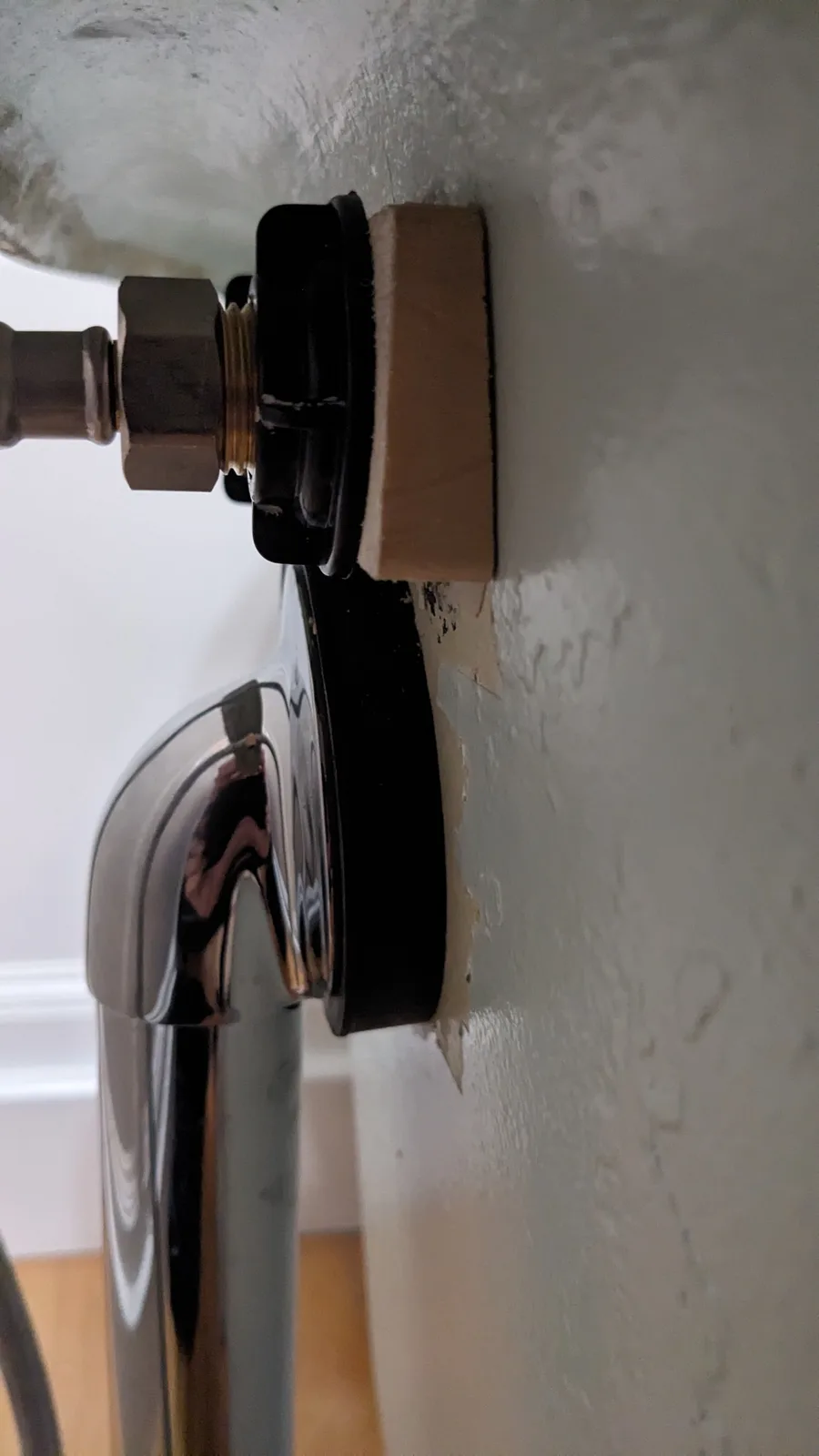 A close-up photo shows a chrome faucet mounted to a wall with visible damage and peeling paint. A small, rectangular piece…