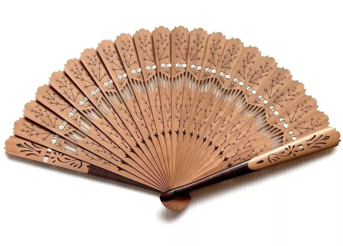 A wooden folding fan with intricate branch-like carvings and silver accents is shown open against a white background. The…