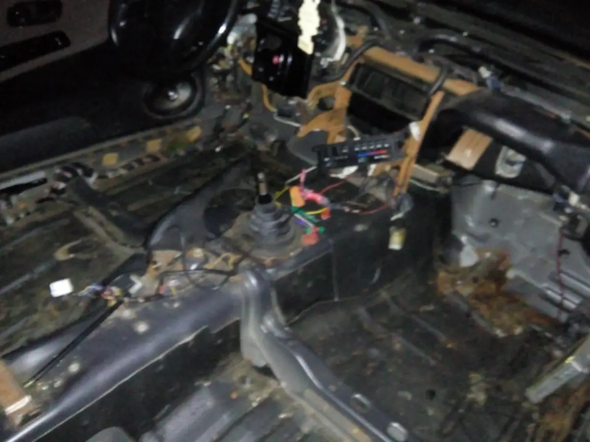 The image shows the interior of a car with its dashboard completely stripped down, exposing wires, metal frames, and a bare…