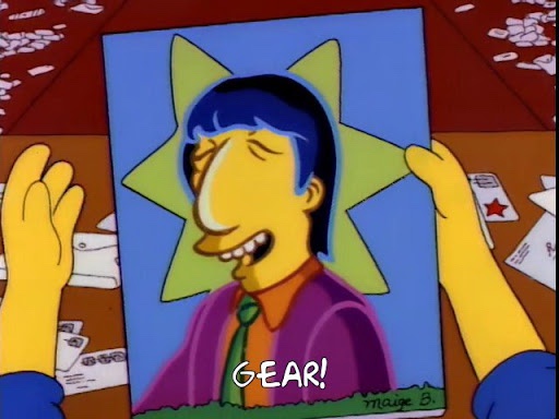 Two yellow hands hold up a framed portrait of a smiling, blue-haired, purple-shirted cartoon man with a green star behind…