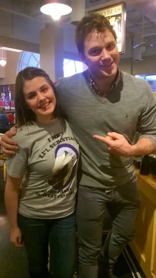 A woman wearing a gray t-shirt with the text 'I MET LIL' SEBASTIAN AT THE FABRE HARVEST FESTIVAL' and an image of a bird…