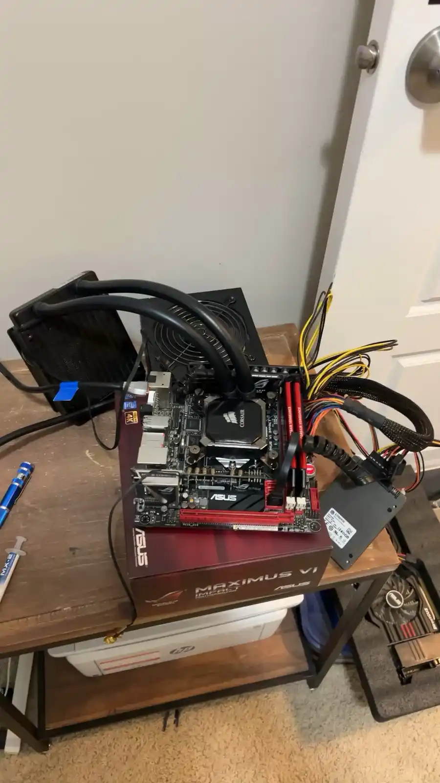 A disassembled computer motherboard sits atop its red and black ASUS Maximus VI Impact retail box on a wooden table…