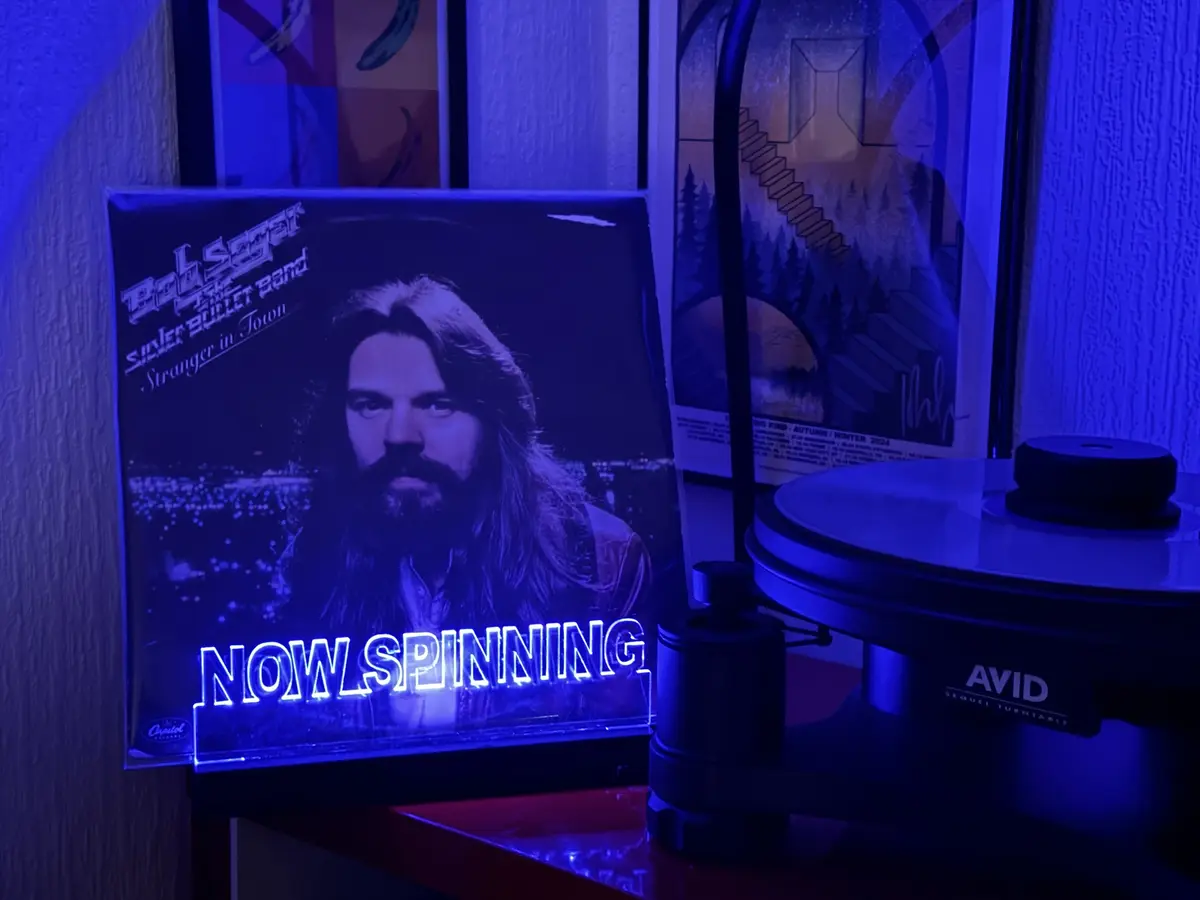 A vinyl record player sits next to a glowing neon sign displaying the album cover of Bob Seger's 'Stranger in Town'. The…
