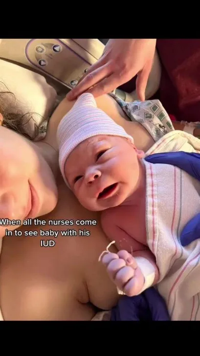 A newborn baby, wrapped in a striped blanket and wearing a white knit cap, lies on a mother's chest. The baby has a small…