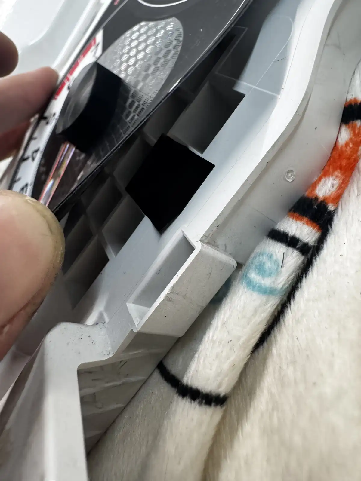 A close-up photo shows a person's fingers manipulating a white plastic component, possibly from a toy or appliance, next to…