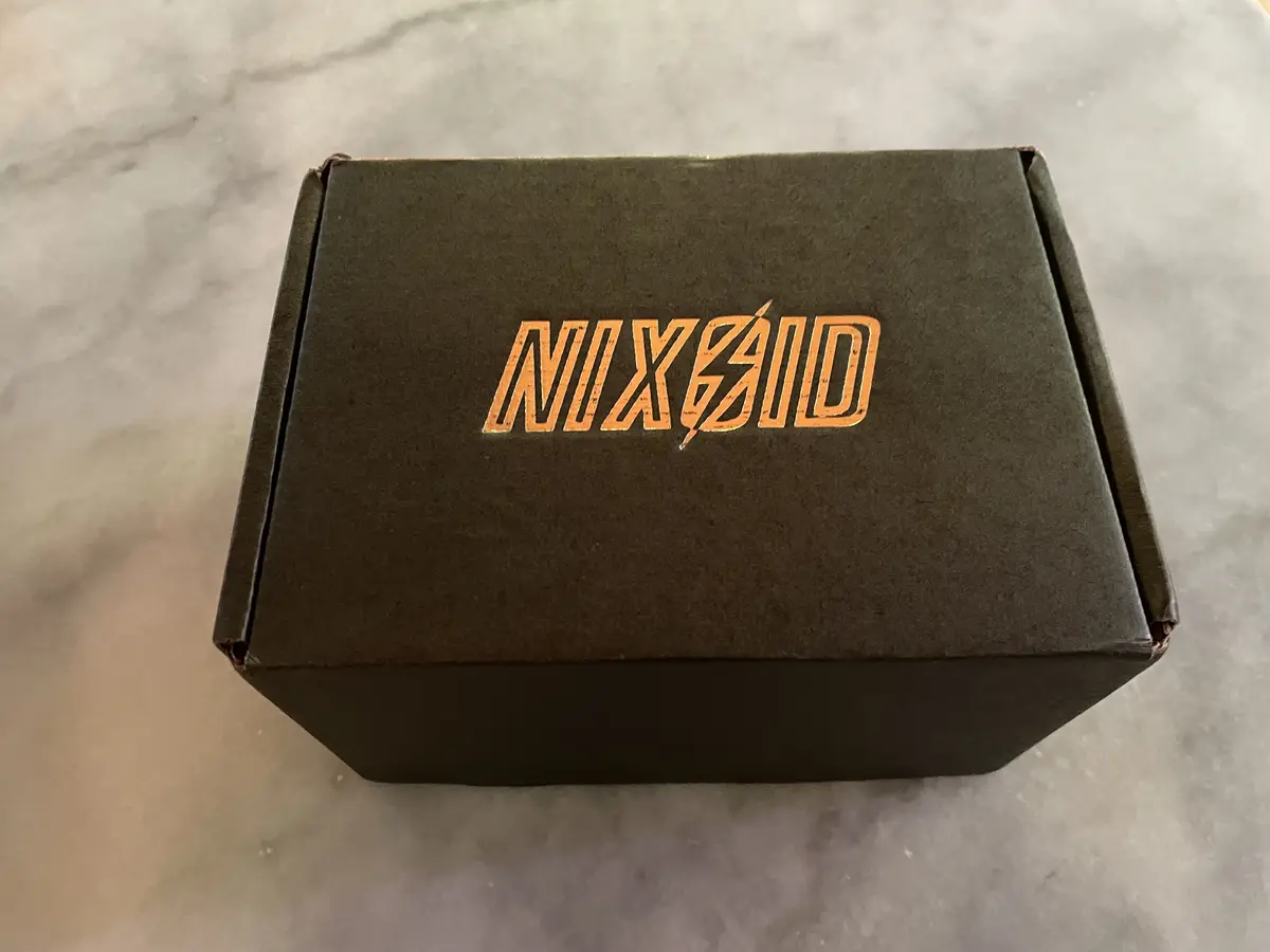 A dark brown cardboard box sits on a light gray marble surface, featuring the word 'NIXSaid' in a stylized orange font with…