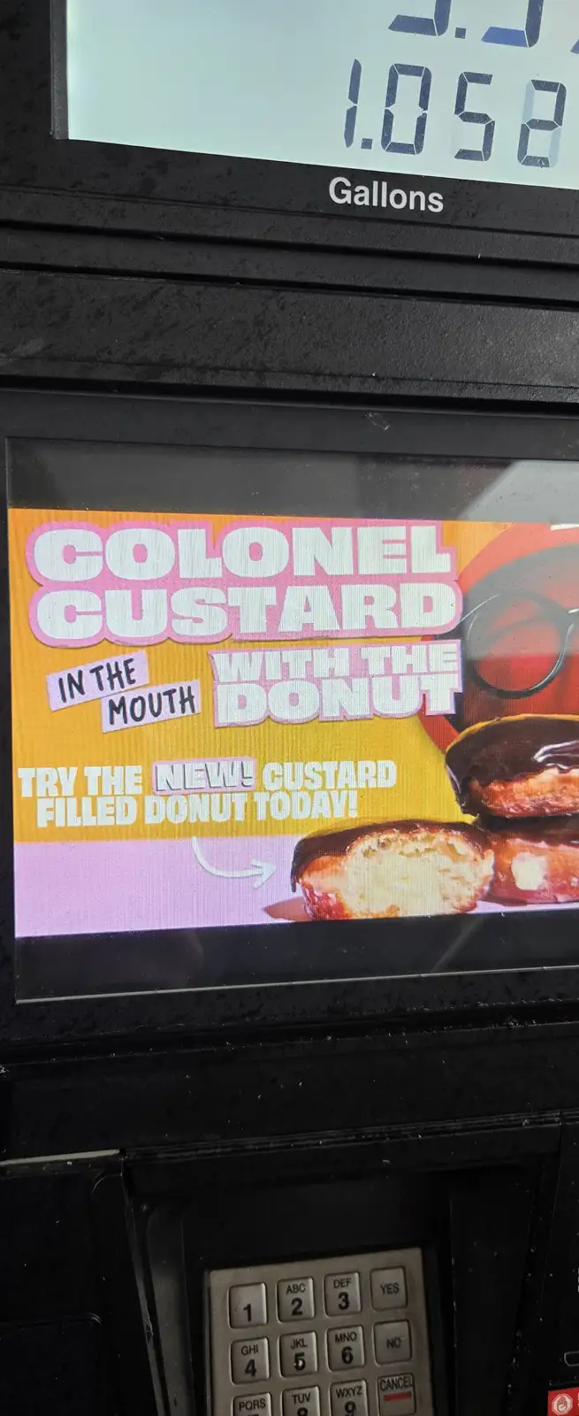 A close-up of a gas pump screen displaying an advertisement for a 'Colonel Custard with the Donut' custard-filled donut…