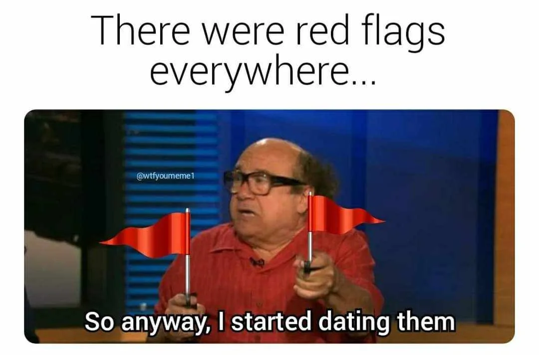 A man in a red shirt and glasses holds two small red flags, looking surprised or confused. The text above him reads 'There…