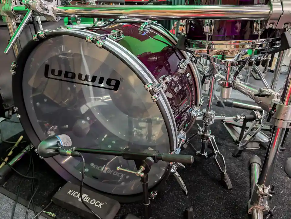 A close-up photo of a Ludwig bass drum with a clear drumhead, featuring a microphone mounted on a stand in front of it and a…