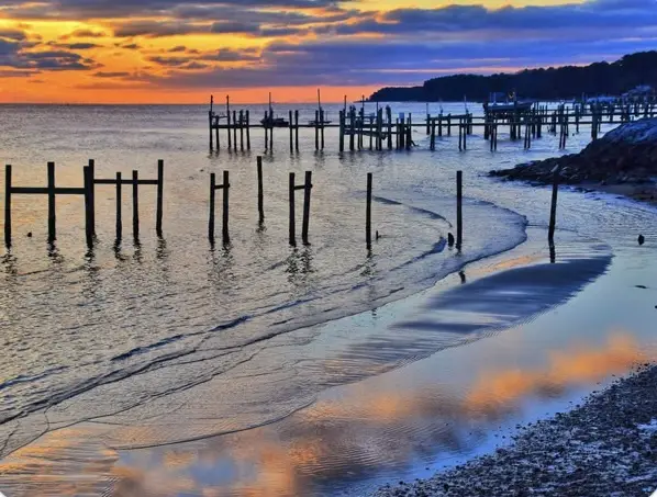 A serene sunset over a beach with wooden pilings and calm water reflecting the orange and blue sky. Overlaid text reads 'i'm…