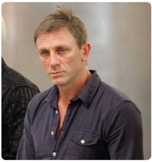 A man with short brown hair and a dark button-up shirt looks directly at the camera with a serious, slightly annoyed…