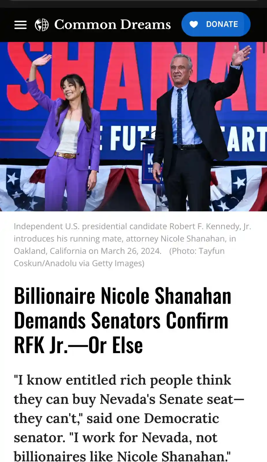 A photo shows two people, a woman in a purple suit and a man in a suit, waving at an event with a large red and blue banner…