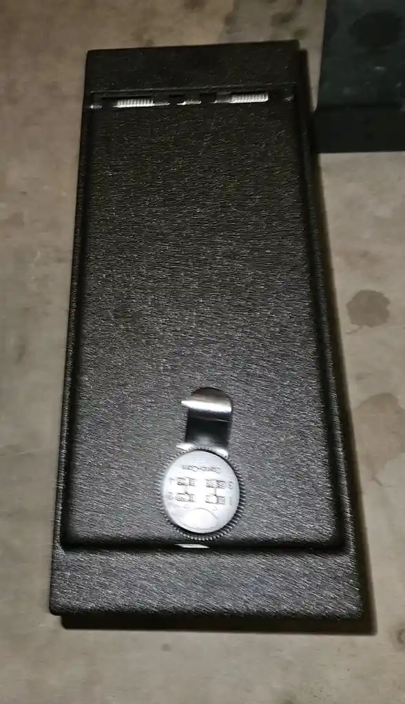 A black, textured, rectangular case with a silver combination lock on its front, resting on a speckled floor. The lock has a…