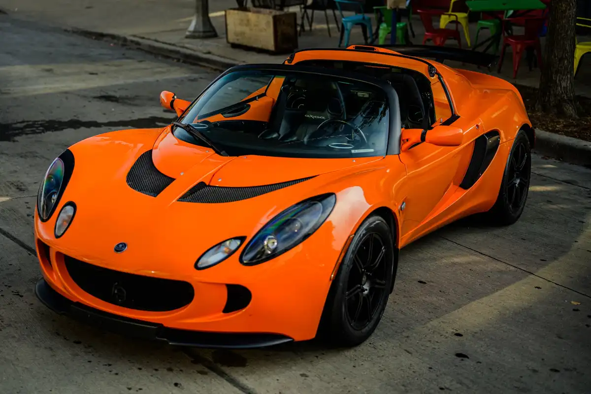 a bright orange lotus exige sports car is parked on a concrete street, its black wheels and carbon fiber accents contrasting…