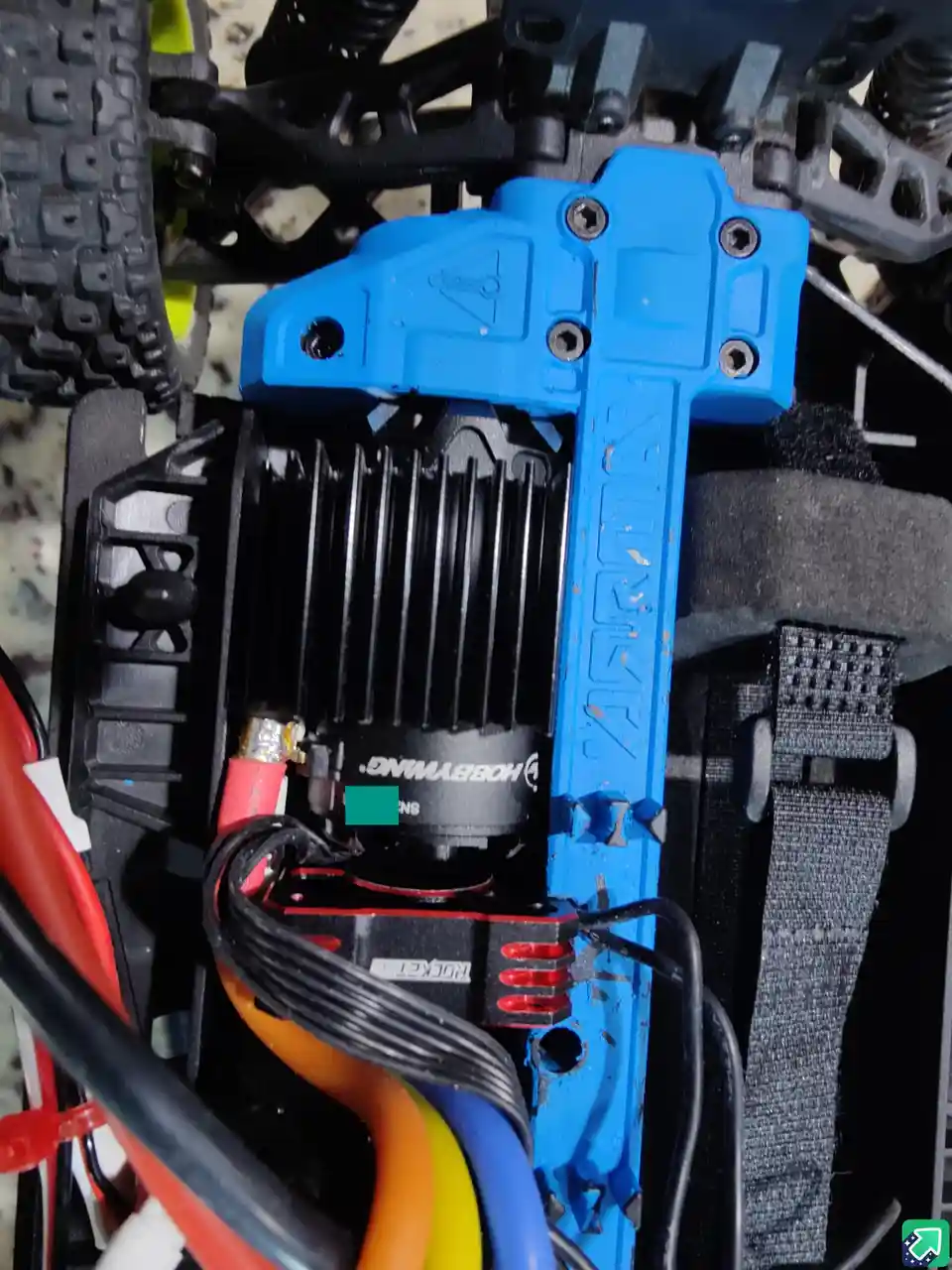 A close-up photo of the internal components of a radio-controlled car, showing a blue plastic chassis, a black…