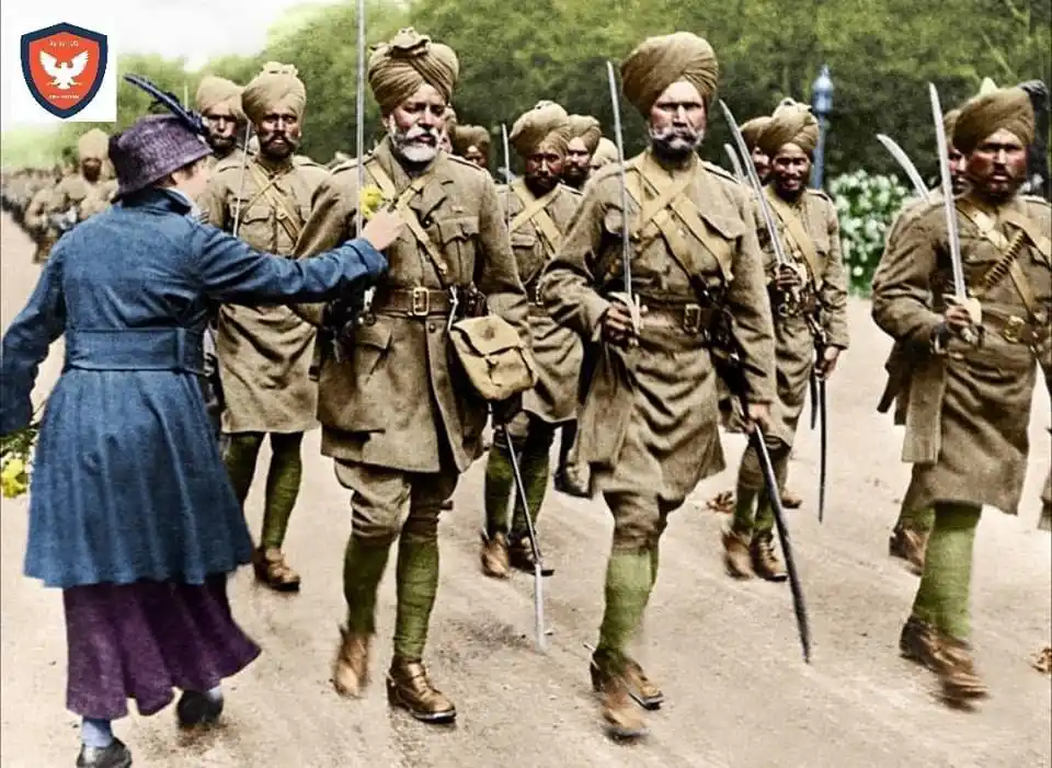 a historical colorized photograph shows a woman in a blue coat and purple skirt offering a yellow flower to a marching…