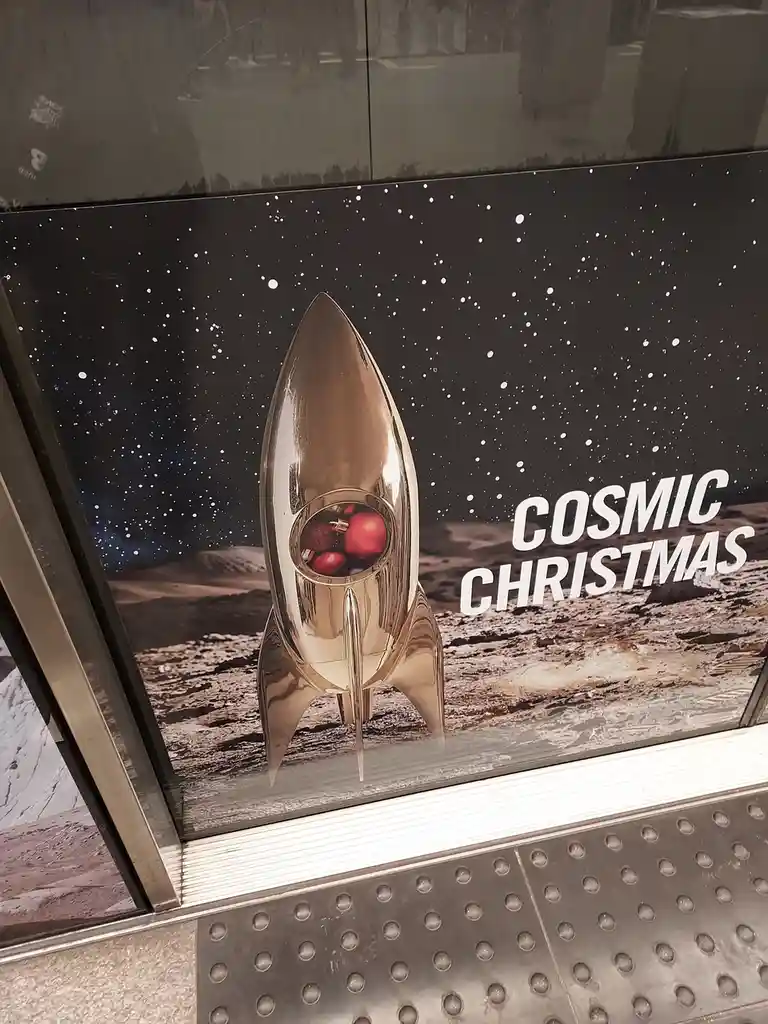 A promotional poster for a 'Cosmic Christmas' event features a shiny, metallic rocket ship sitting on a barren, rocky planet…