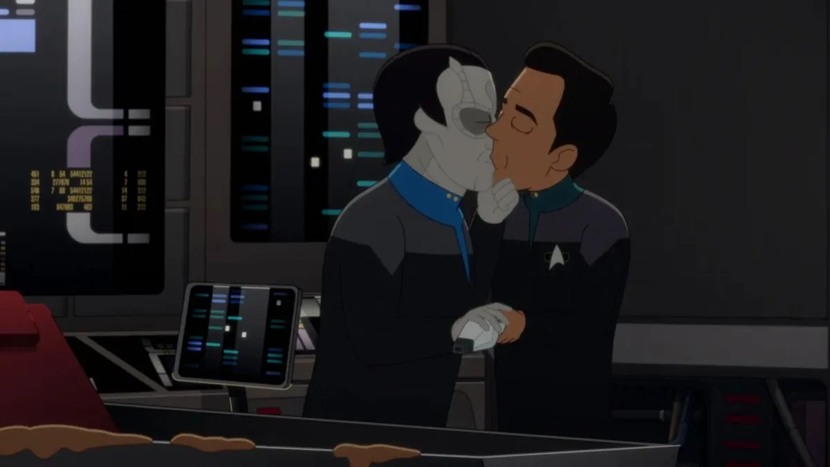 Two animated characters in Starfleet uniforms are kissing in a spaceship control room filled with glowing screens and…