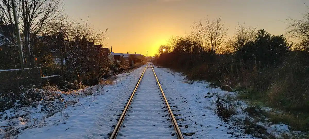 A snowy railway track stretches toward a setting sun, flanked by bare trees and houses, with overlaid text reading 'i'm not…