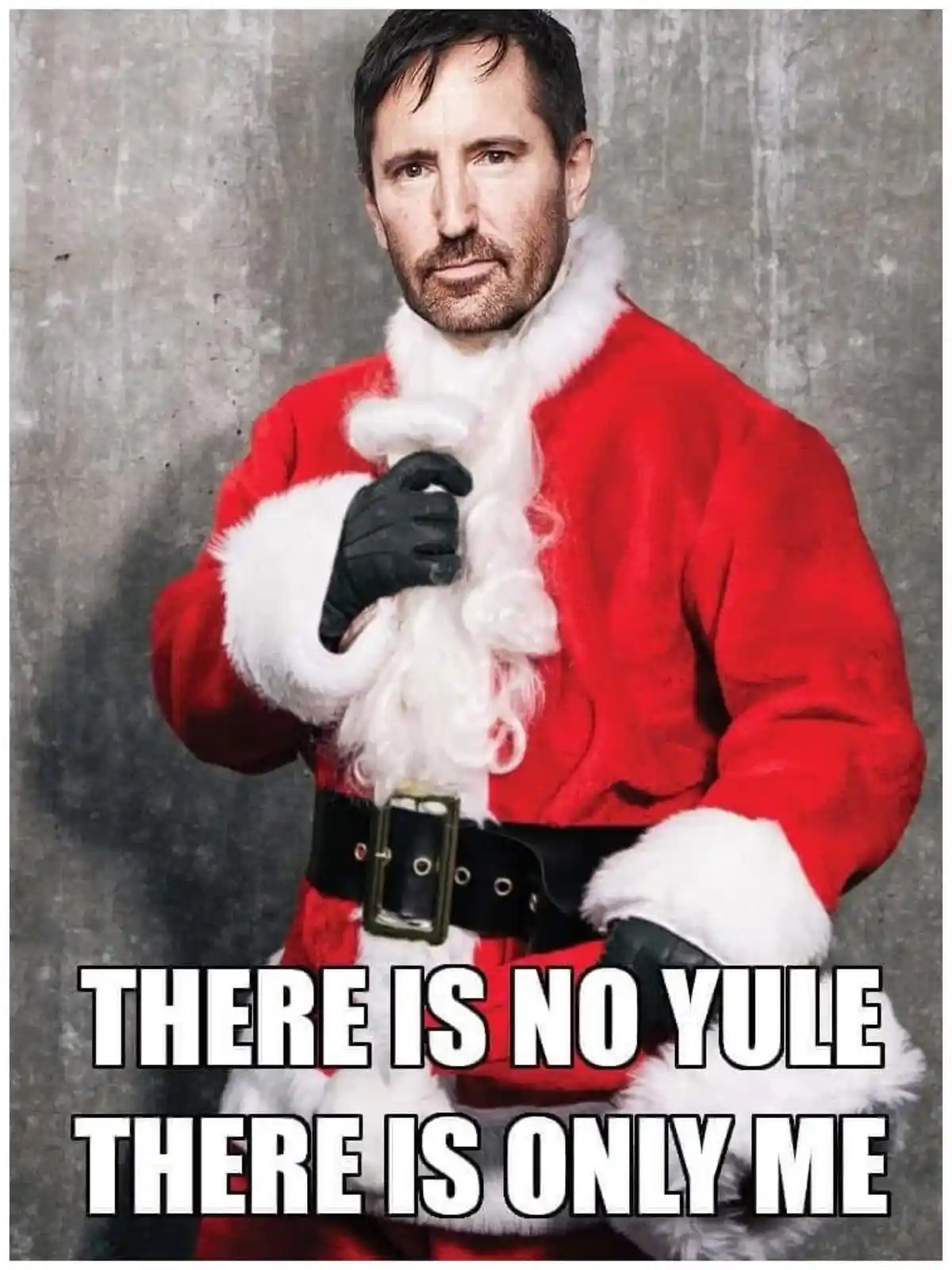 A man with a serious, intense expression is dressed in a red Santa suit with white fur trim and black gloves, holding a…