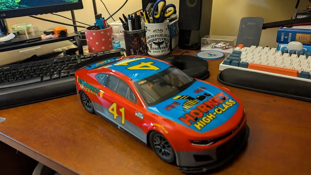 A red and blue toy race car with the number 41 and "Hornet High-Class" text on its side sits on a cluttered desk next to a…