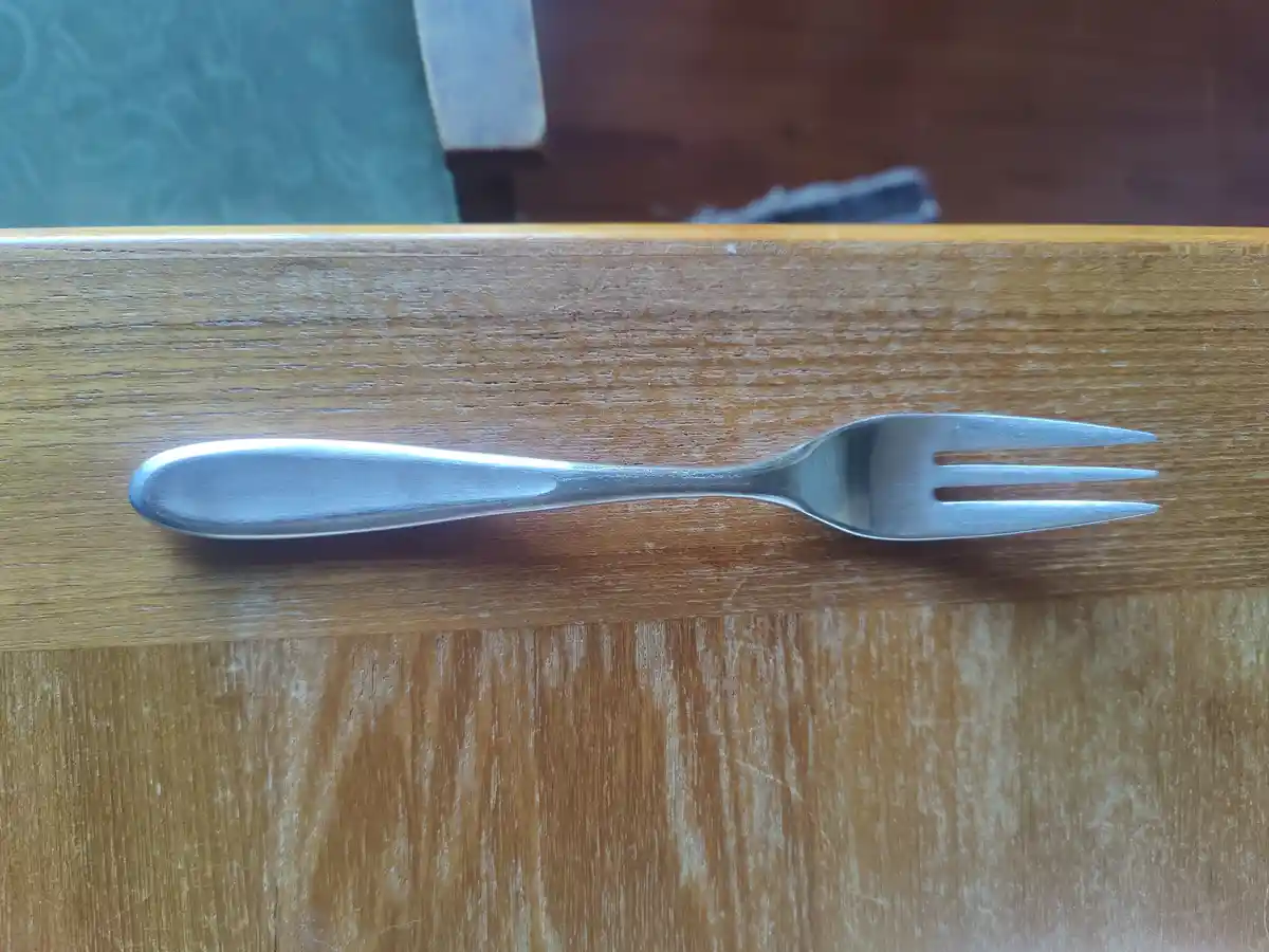 A silver, three-pronged fork lies horizontally on a worn wooden table surface. The overlaid text reads 'i'm not a fork, i'm…