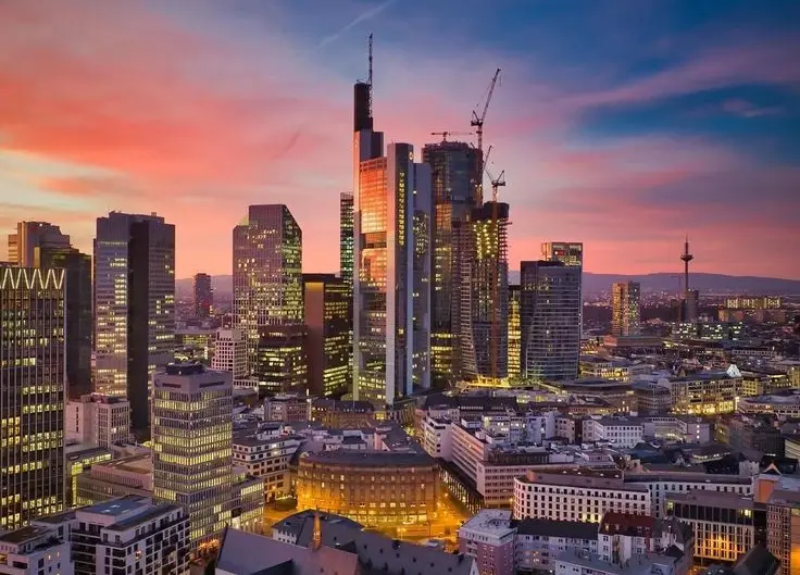 A vibrant cityscape at sunset, featuring modern skyscrapers with lit windows against a pink and orange sky, overlaid with…