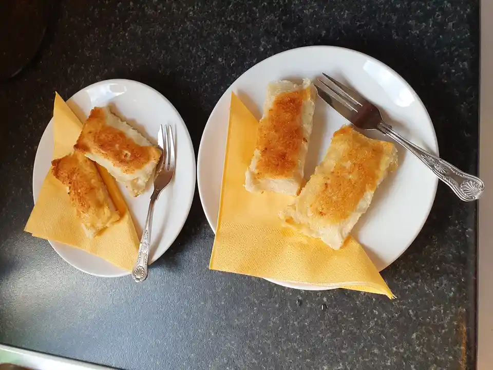 Two white plates sit side by side on a dark countertop, each holding two golden-brown fried rice cakes resting on yellow…