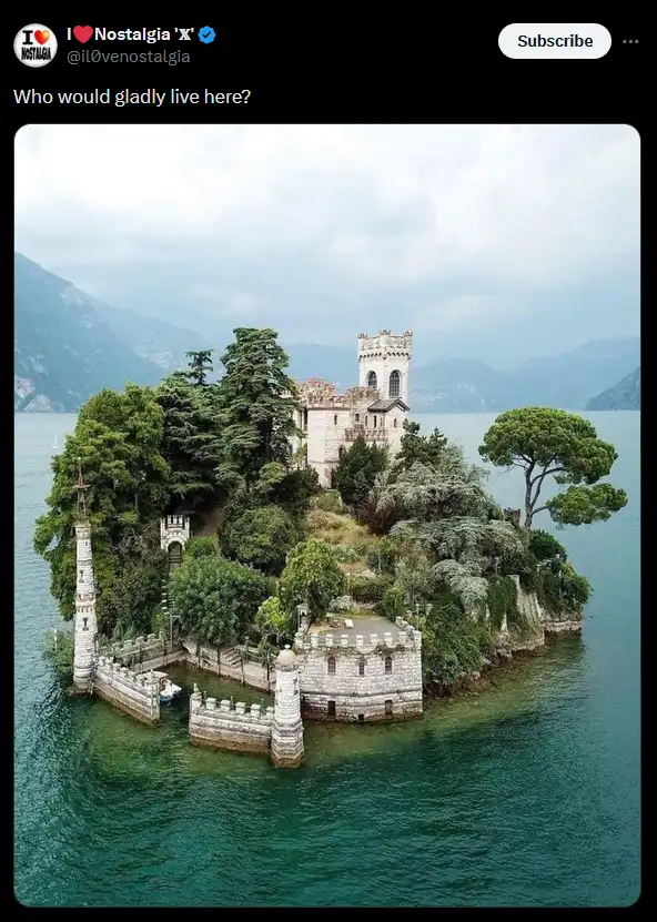 An aerial photo shows a small, lush island in a lake surrounded by mountains, featuring a stone castle with turrets and a…