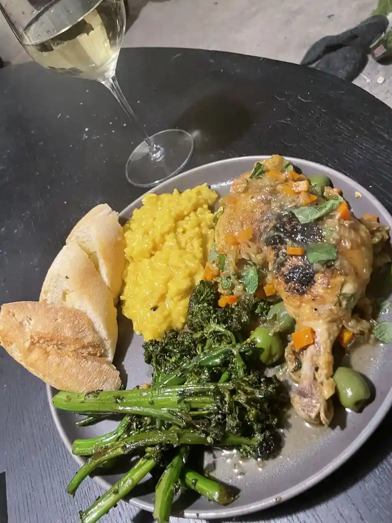 A plate of home-cooked dinner featuring a roasted chicken leg with vegetables, yellow rice, and broccolini, accompanied by…