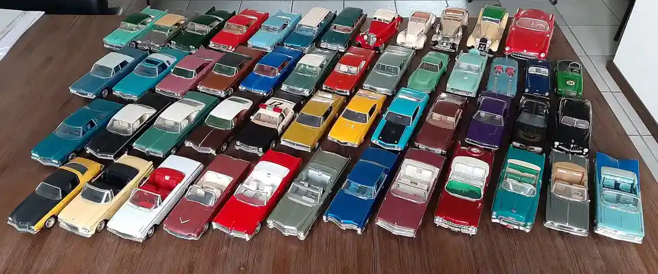 An overhead shot displays a large collection of vintage diecast model cars arranged in neat rows on a wooden table. The cars…