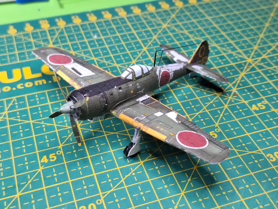 A detailed scale model of a Japanese World War II fighter plane, featuring red circle insignias and weathered camouflage…