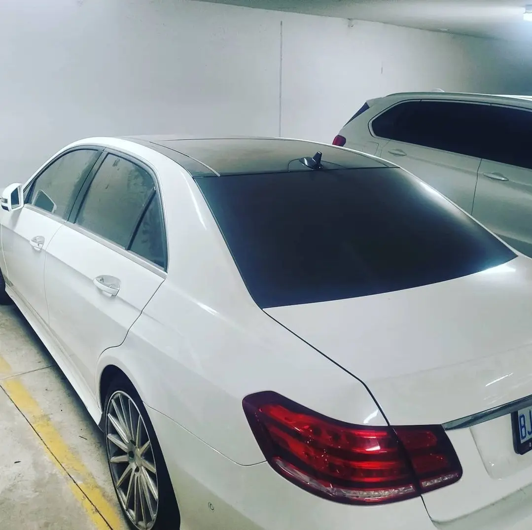 A white luxury sedan is parked in an underground garage, its rear window covered in a dark tint. The car's taillights and…