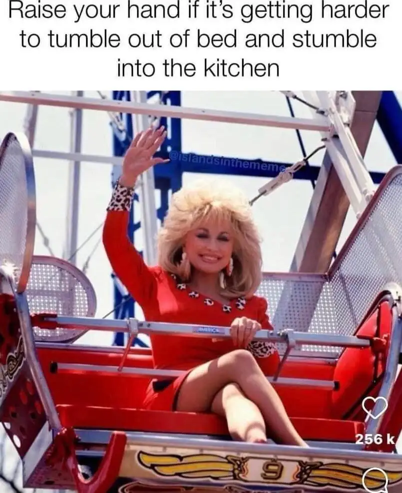 A woman with blonde hair wearing a red dress and leopard-print cuffs sits in a red amusement park ride car, smiling and…