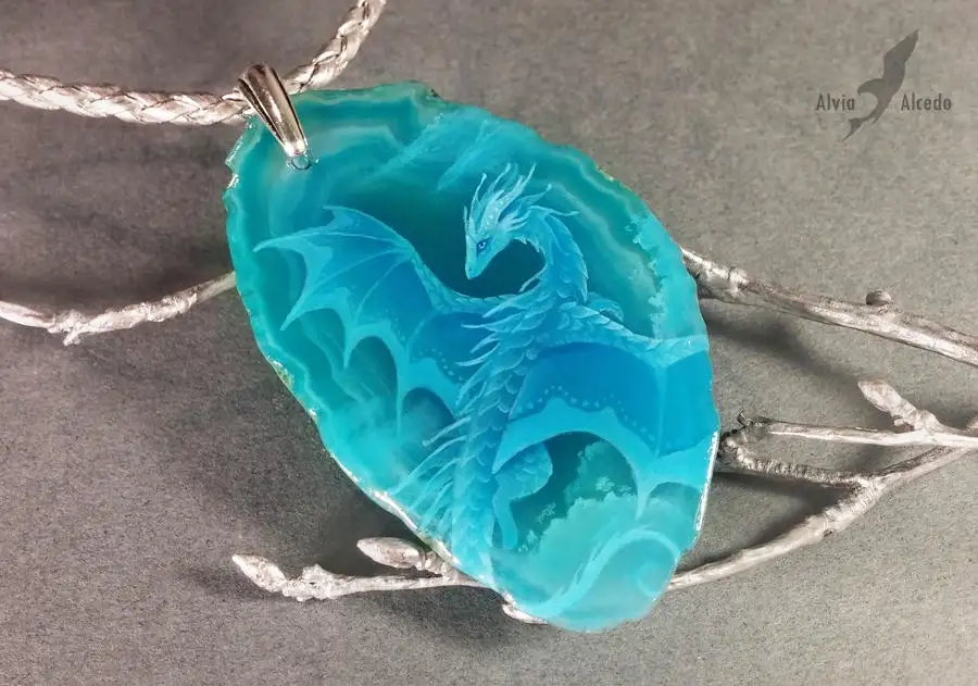 A close-up photograph of a turquoise-blue agate pendant with a detailed dragon carved into its surface, hanging from a…