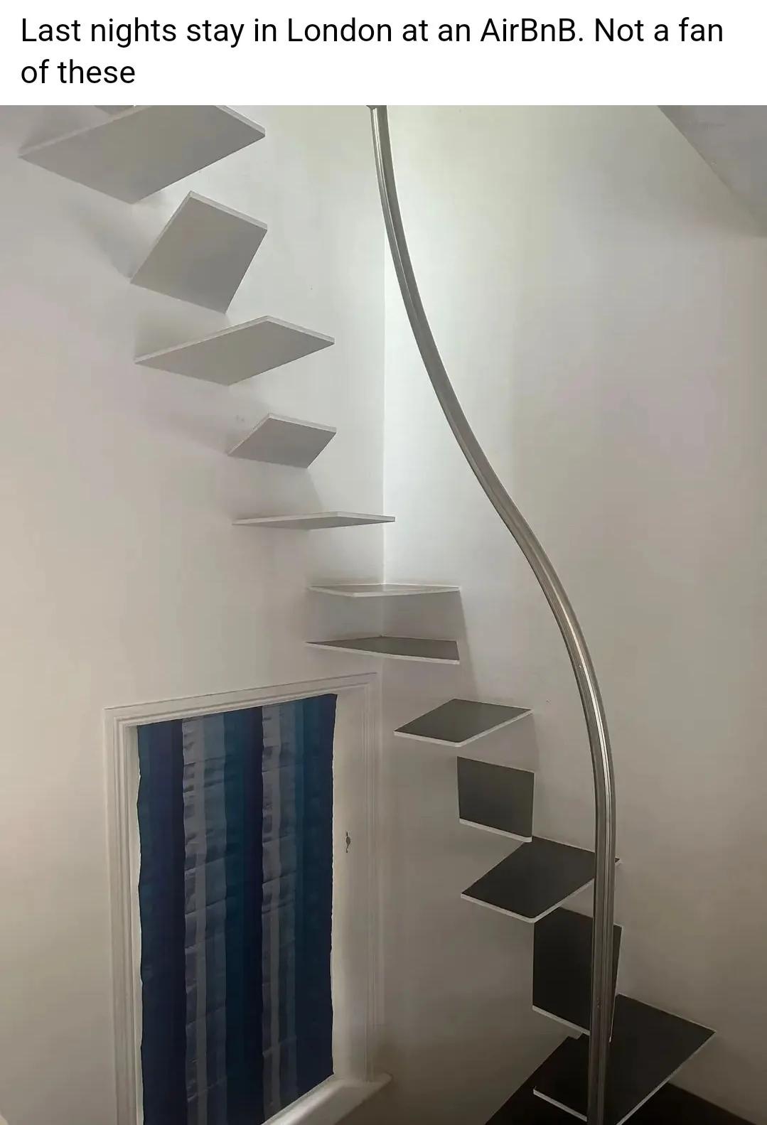 A photo shows a modern, minimalist spiral staircase with white walls and a curved metal handrail. The steps are flat…