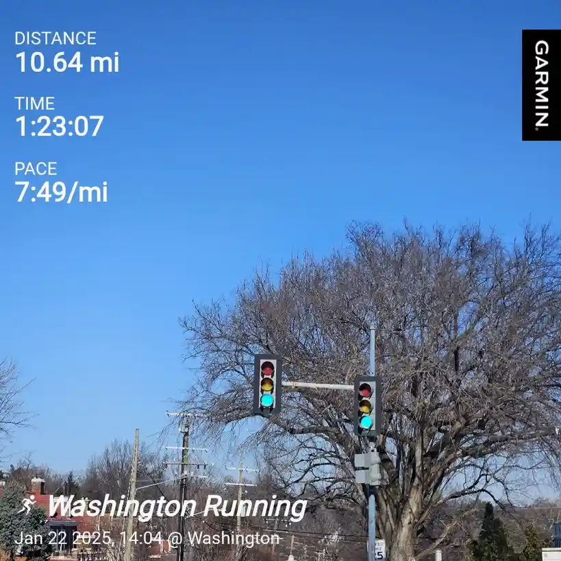 A Garmin running app screenshot overlaying a photo of a traffic light with green illuminated, showing stats for a 10.64-mile…